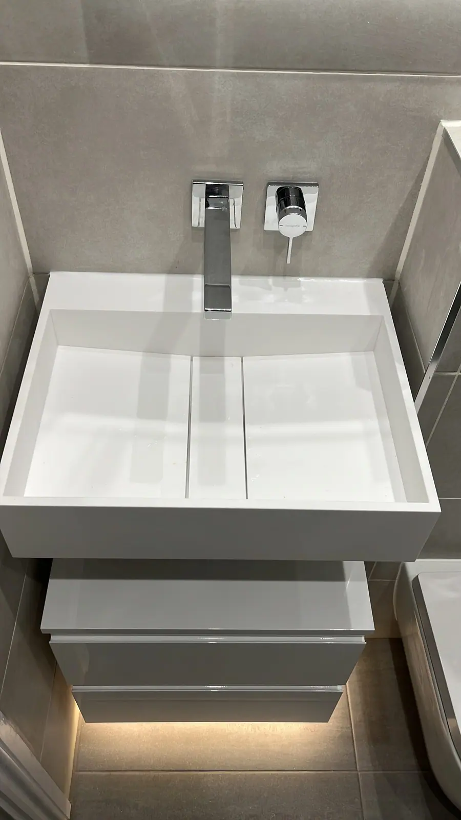 The wall-hung basin with wall-mounted tap and a lit drawer unit below