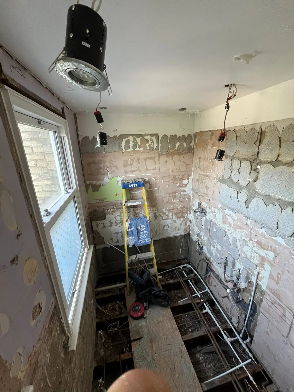 The bathroom stripped back to brick and joists, with new pipework running across the floor