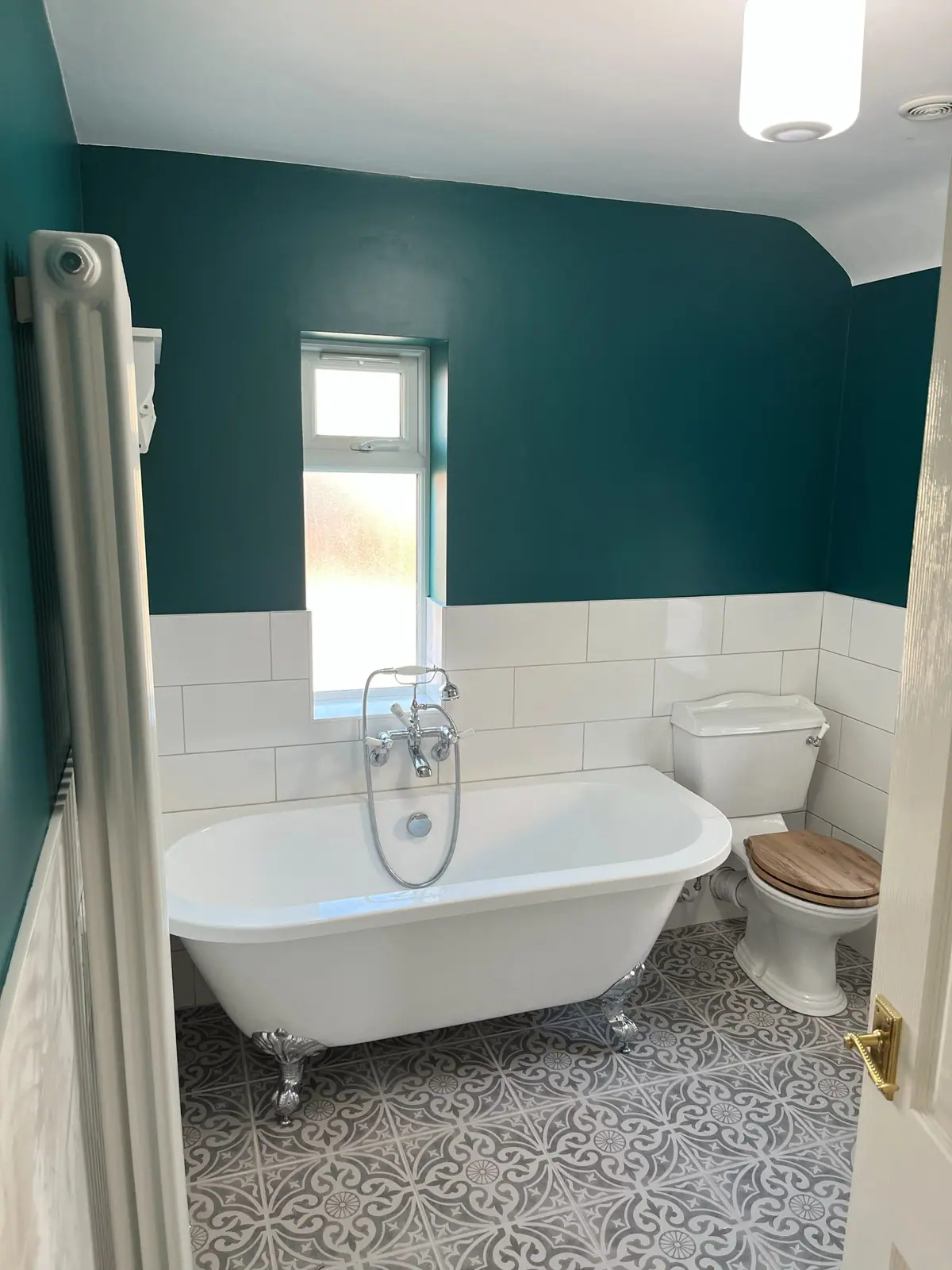 A roll-top bath under the window with white metro tiles and a patterned floor