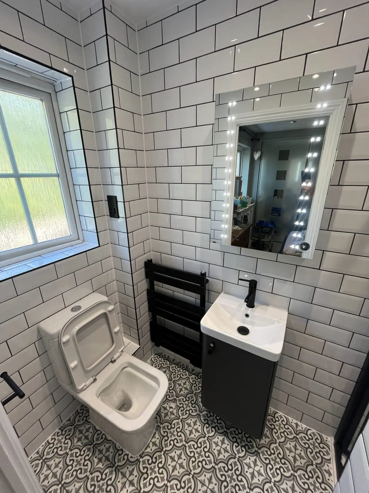 A compact shower room with metro tiles, a patterned floor and a black towel radiator
