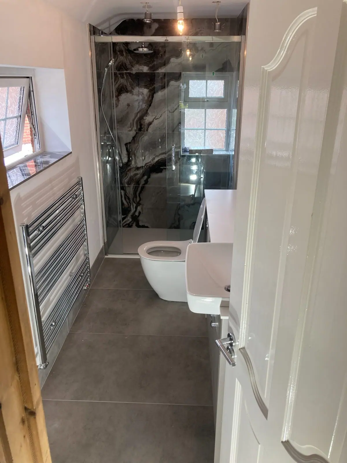 The same room refitted with a walk-in shower, marble-effect wall panels, a heated towel rail and a wall-hung toilet