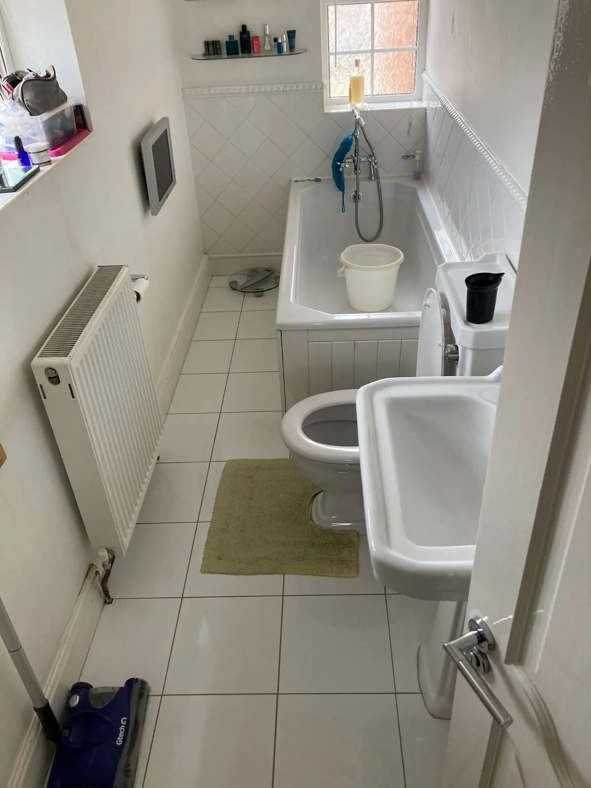 A dated bathroom with a panelled bath, white wall tiles and a radiator under the window