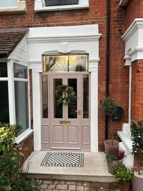 The new panelled front door painted pink, with a fanlight above and a tiled step