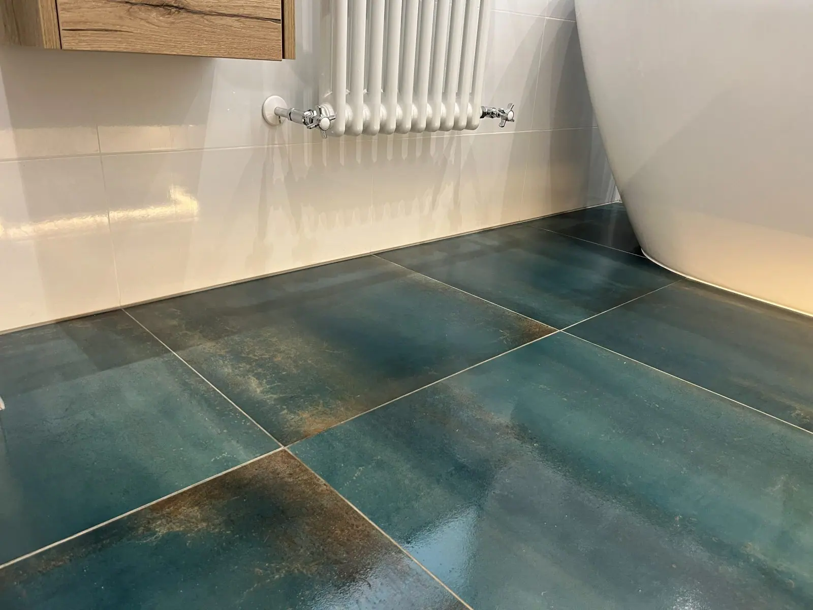 Large-format teal floor tiles in a finished bathroom around a freestanding bath