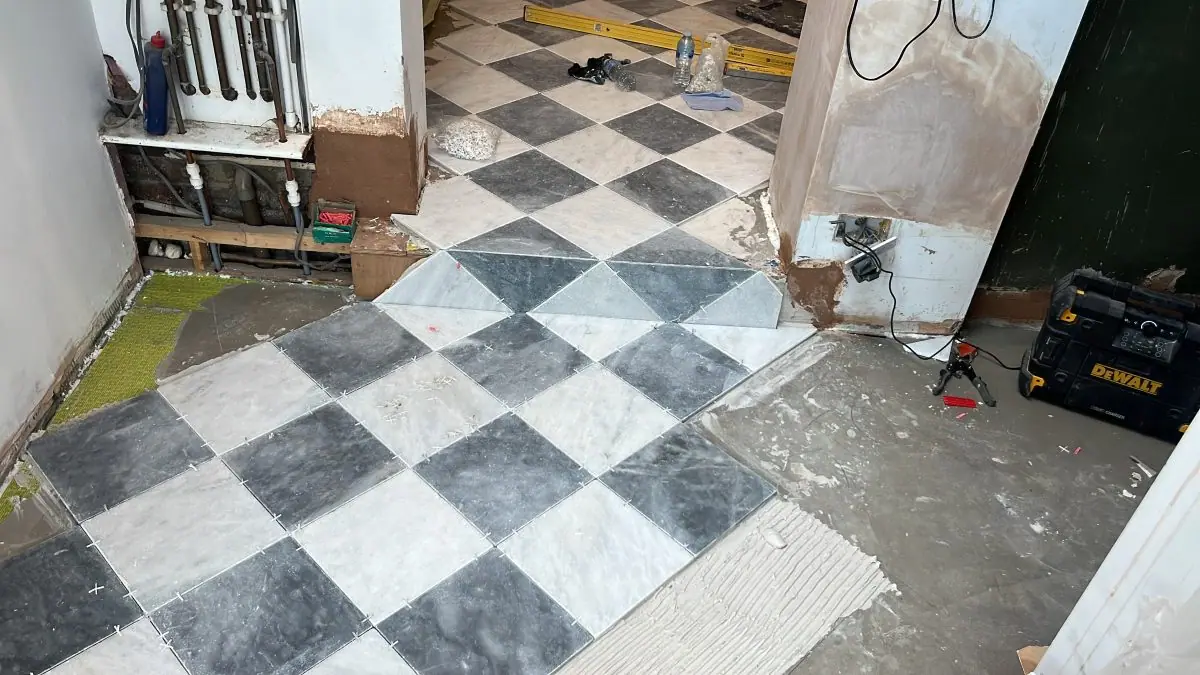 Black and white stone floor tiles being laid on the diagonal over a levelled screed