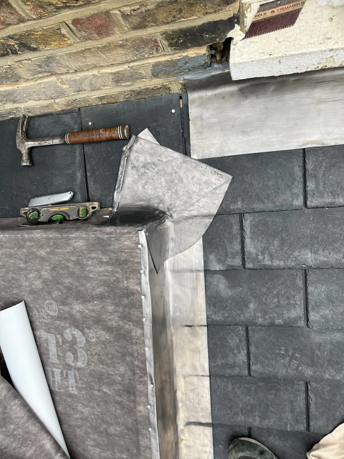 Lead flashing being dressed into place where a slate roof meets a wall