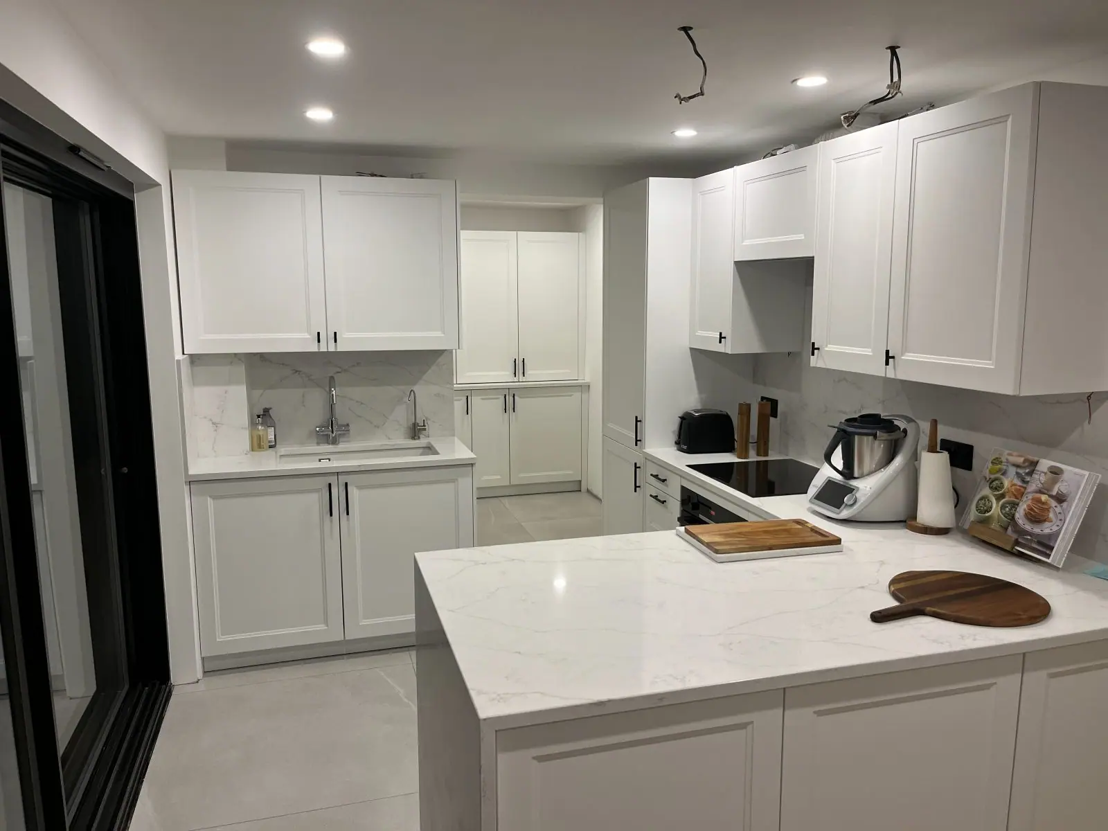 A white shaker kitchen with a quartz-topped peninsula and tall larder units
