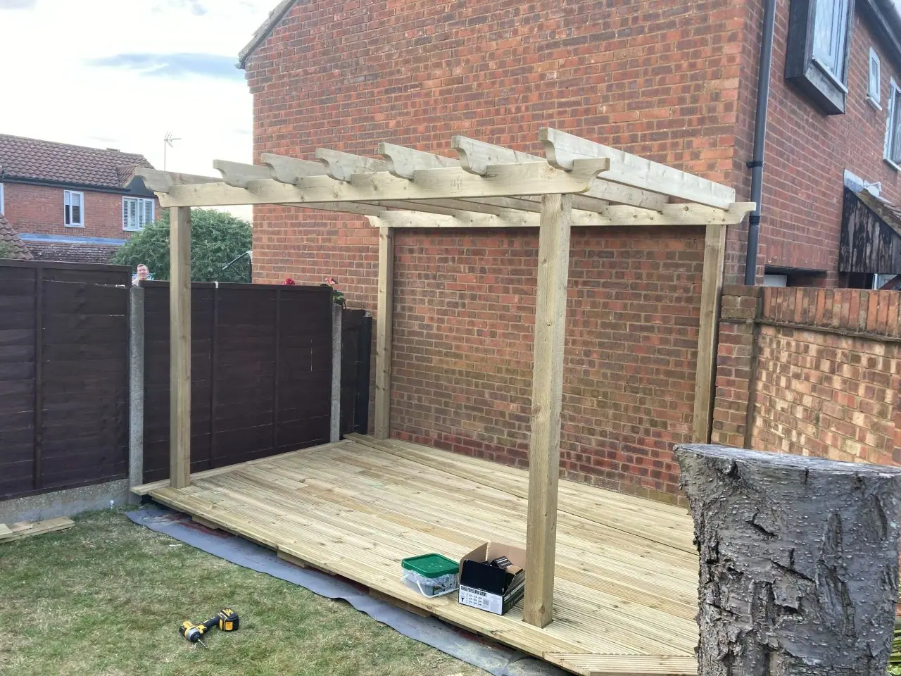 The finished deck with a pergola built over it against the brick wall