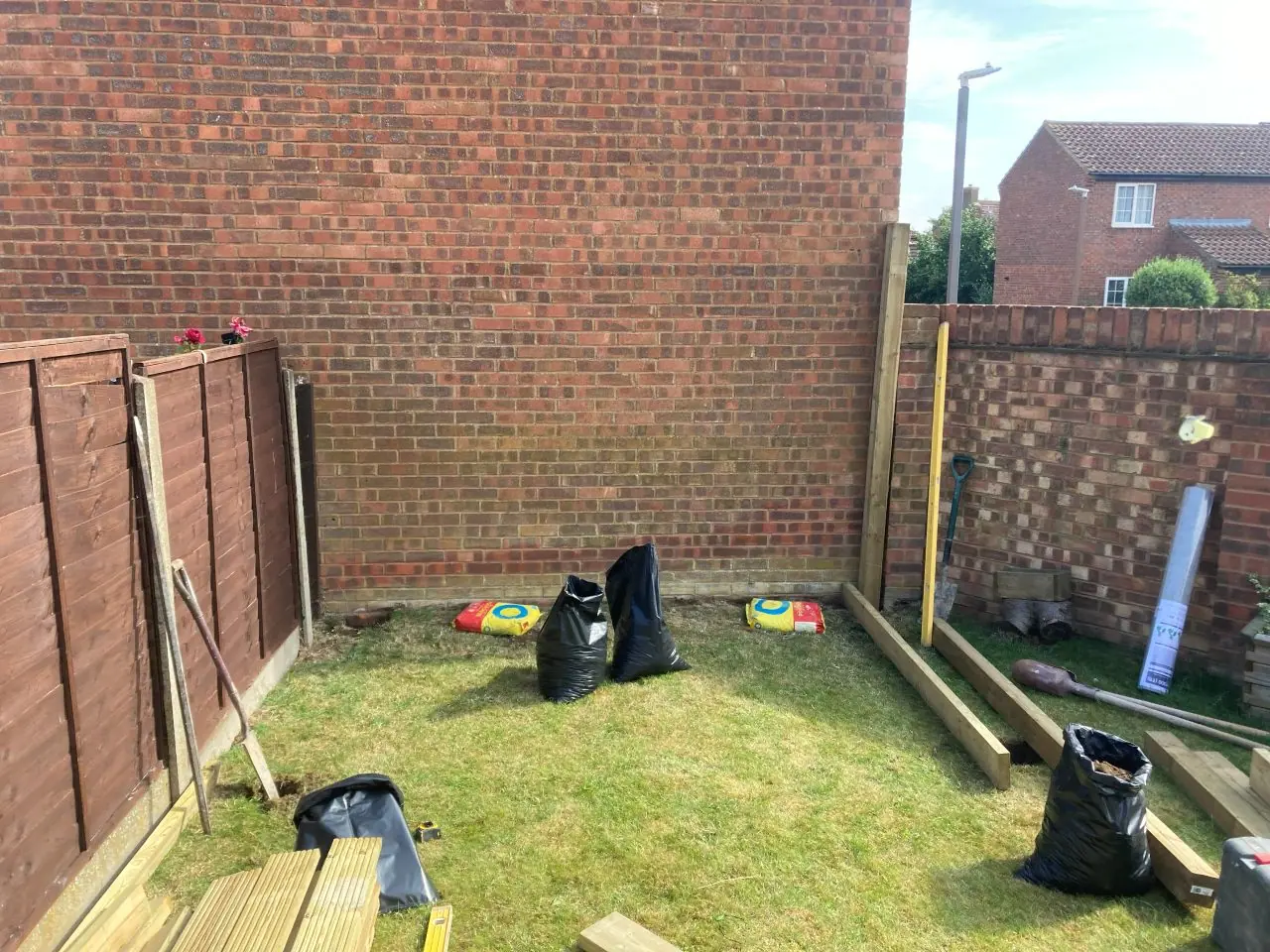 The corner of the garden cleared back to grass, with timber stacked ready