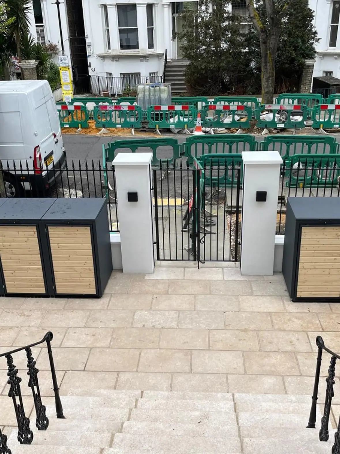 A front garden paved in pale stone, with rendered gate piers and timber-clad bin stores