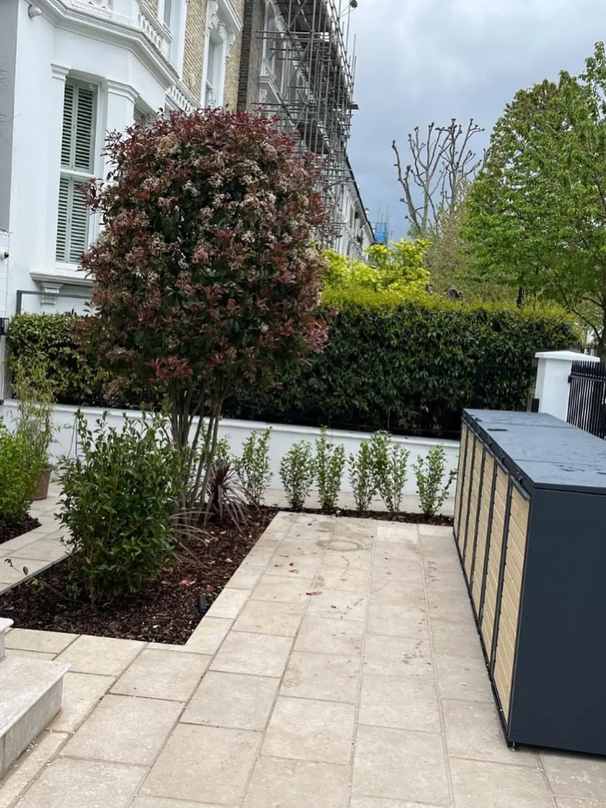 The paved front garden with a raised planting bed and a bin store