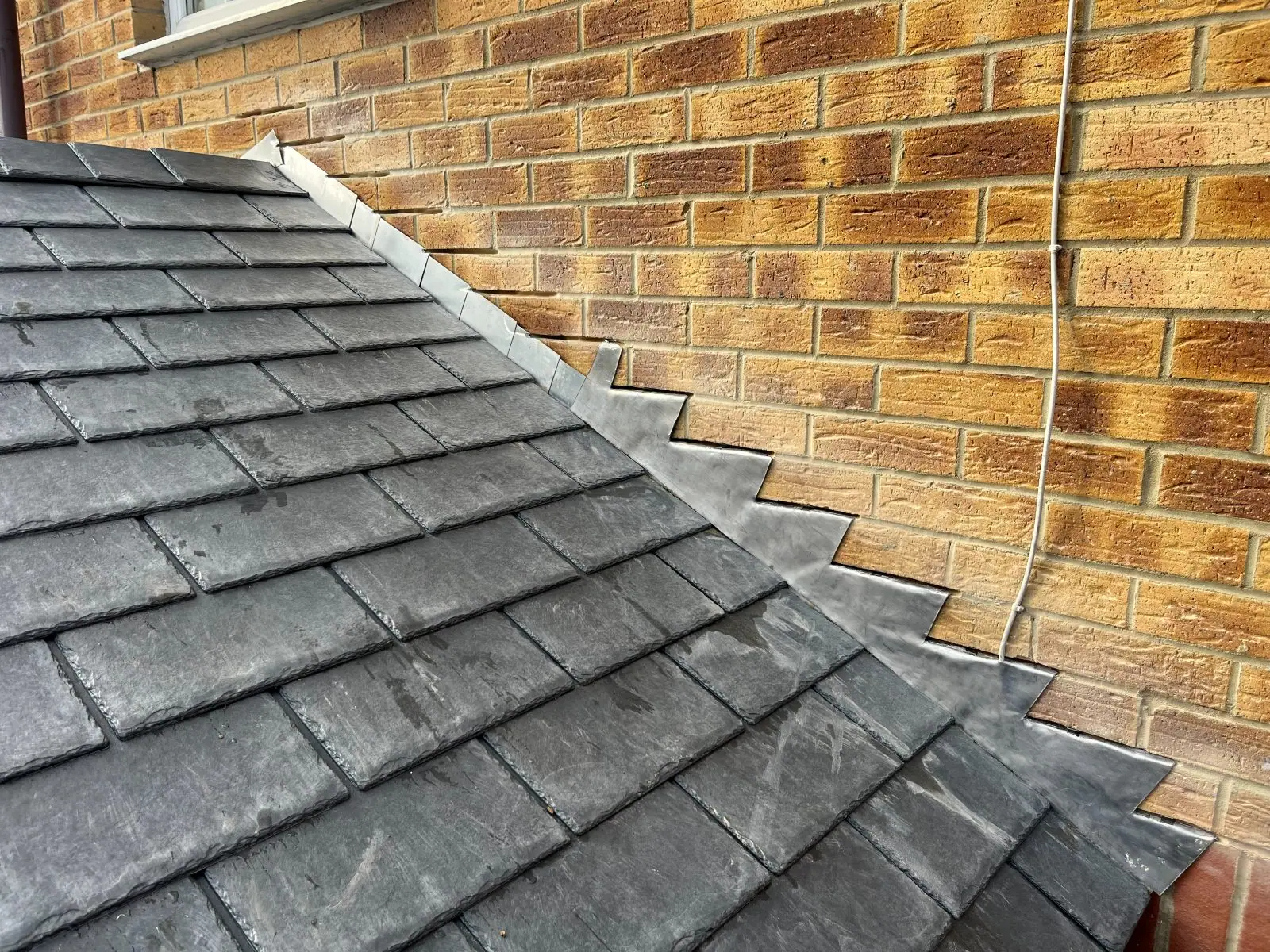 Stepped lead flashing cut into the mortar joints of a brick wall above a slate roof, with soakers turned up behind each course
