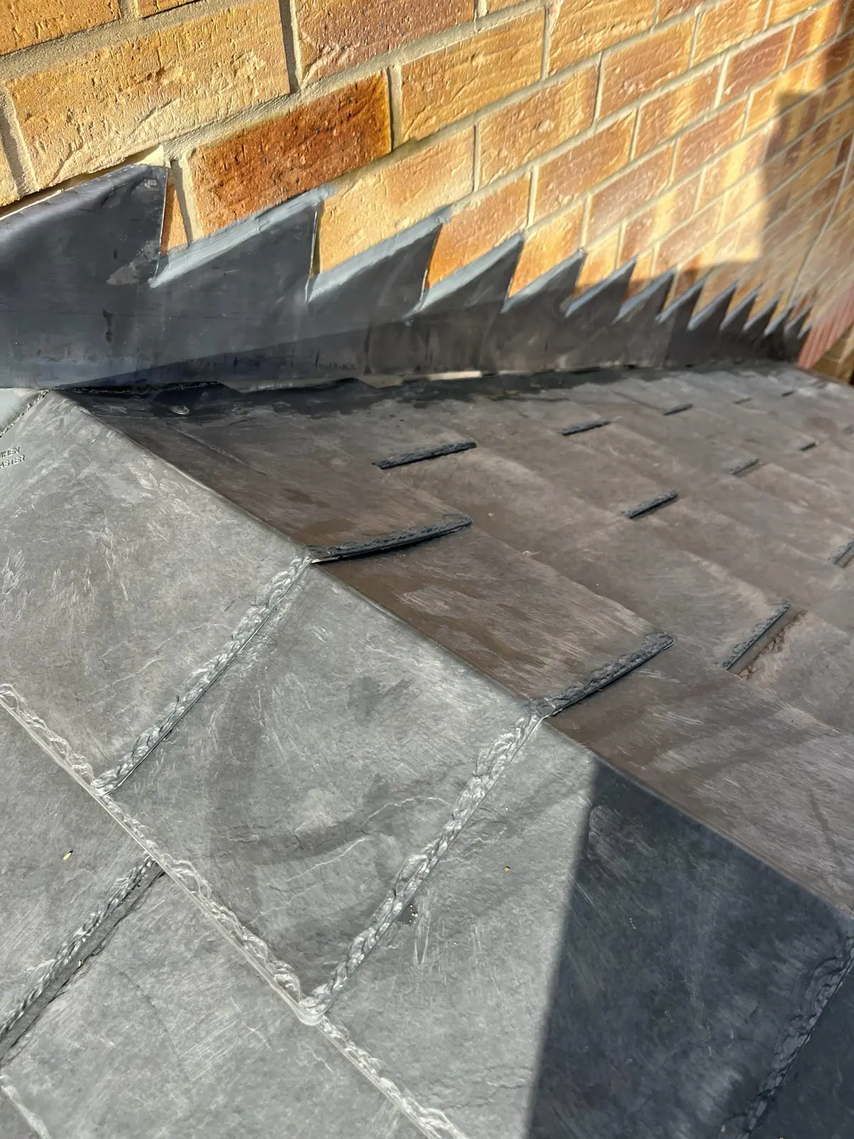 Lead apron and stepped flashing dressed over the hip of a slate roof where it meets the wall
