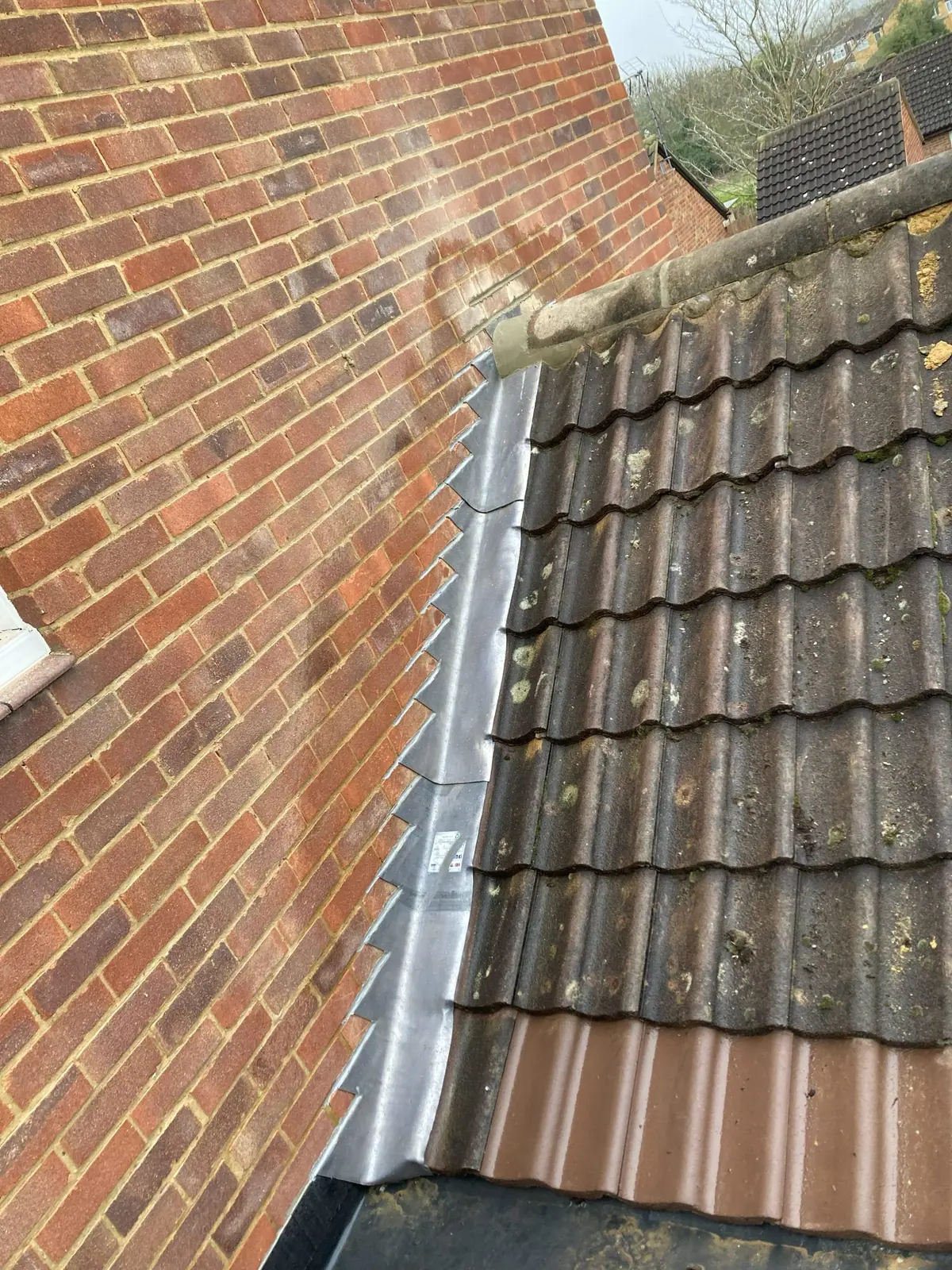 New stepped lead flashing running up a brick gable beside an interlocking-tile roof