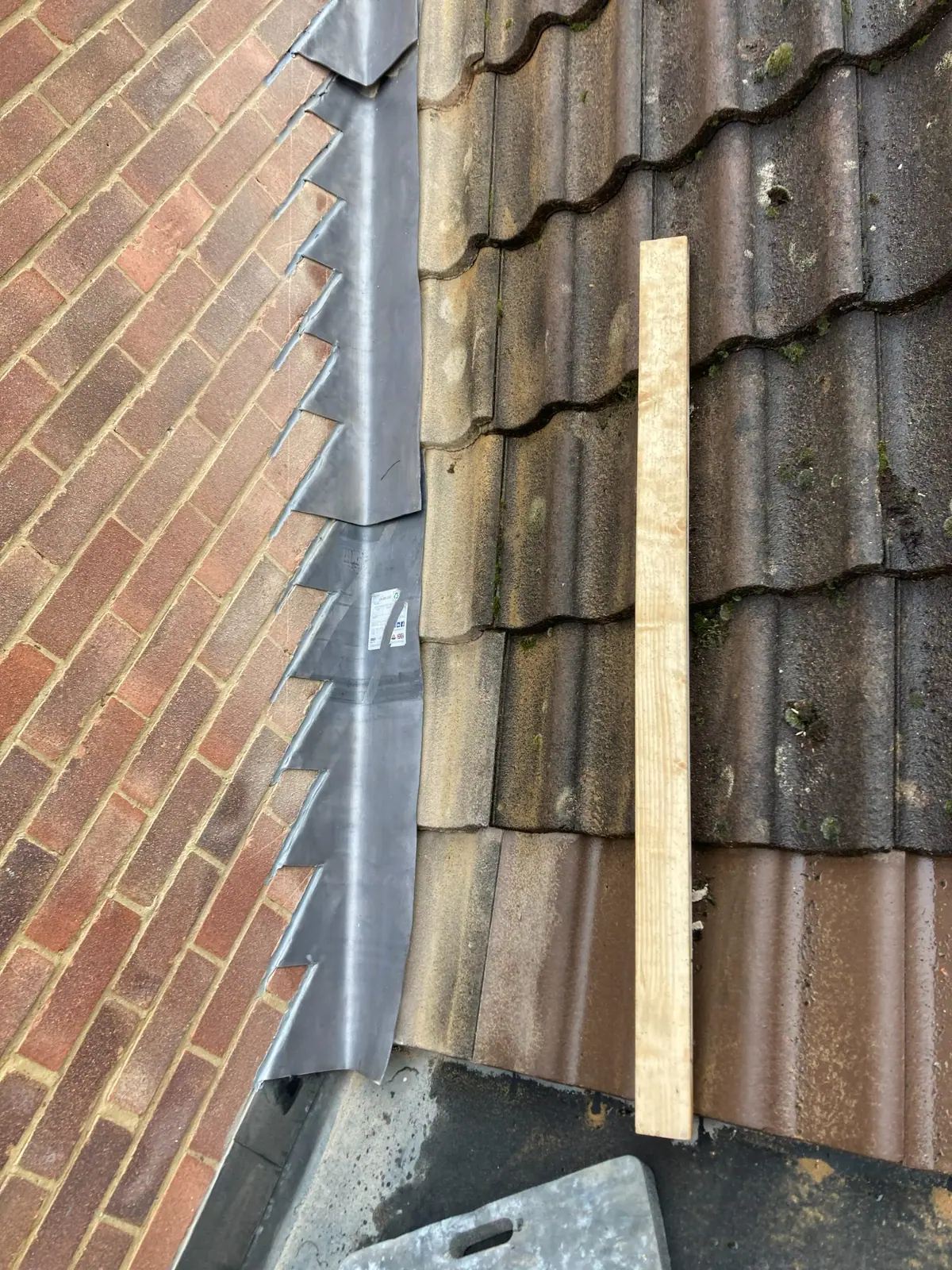 Close view of the new stepped flashing cut into the brick courses, with the lead dressed over the tiles